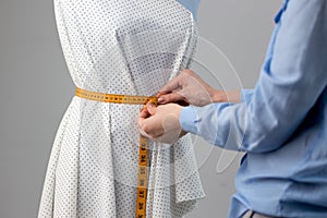 Seamstress measuring beautiful fabric on blue tailor dummy in her workshop.