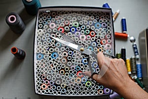 A seamstress pulls a pair of scissors out of a box with skeins of colored threads.Sewing industry