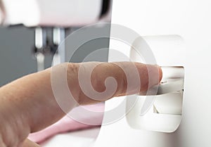 A seamstress& x27;s finger switches the reverse key of a sewing machine while sewing, close-up. Industry, regulator