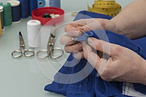 Seamstress sews the button to a blue pants