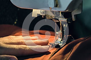 Seamstress sews clothes made of red cloth on a sewing machine