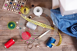 Seamstress or tailor background top view with jeans, sewing tools, colorful threads, sewing machine and accesories .
