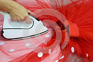 A seamstress with a white iron strokes a red tulle skirt with white satin circles