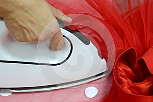 A seamstress with a white iron strokes a red tulle skirt with white satin circles