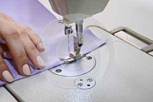 Seamstress works on a sewing machine. The girl sews and holds a lilac cloth