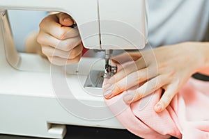 Seamstress works on a sewing machine. The girl sews and holds a pink cloth