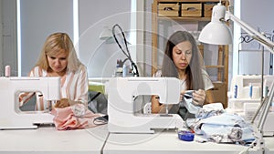 Seamstresses at work in workshop sewing clothes near sewing machine, front view.