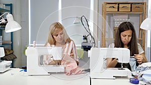 Seamstresses at work in workshop sewing clothes near sewing machine, front view.