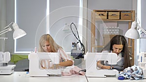 Seamstresses at work in workshop sewing clothes on sewing machine, side view.