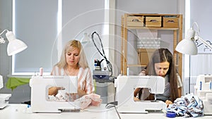 Seamstresses at work in workshop sewing clothes on sewing machine, side view.