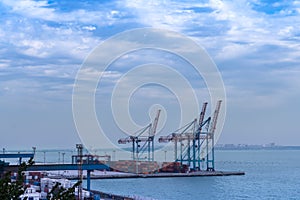 Seaport area, large cranes and stacked shipping containers against the backdrop of the sea