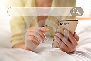 Search bar of internet browser and woman using smartphone on bed, closeup