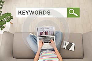 Search bar with text KEYWORDS and woman with laptop on sofa
