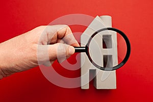 Search for housing for rent. House miniature and magnifying glass on a red background. Dangerous buying of real estate