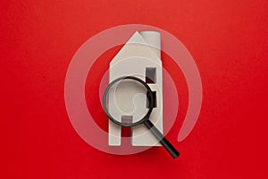 Search for housing for rent. House on a red background with a magnifying glass. Expertise of real estate