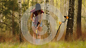 Search with a metal detector. Young woman digging detected metal in the forest