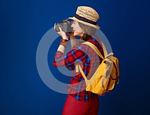 Tourist woman isolated on blue with DSLR camera taking photo