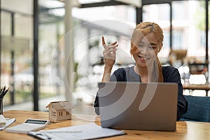 Searching the internet for real estate or new house with model home and key, young asian woman using laptop computer.