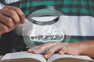 Searching and learning concept.male hand holding a magnifying glass looking at a book lying on the table with a picture of a brain