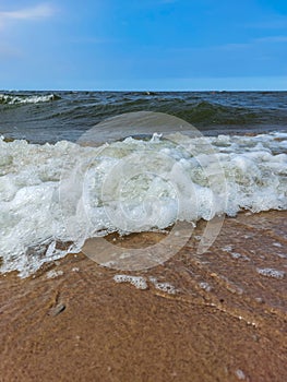 Seascape of the Baltic sea with big foamy waves with yellow sand on the shore and clear blue sky above