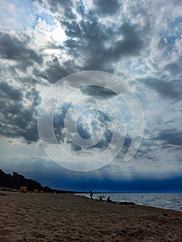 Seascape of the Baltic sea with big foamy waves with yellow sand on the shore and very dark, blue, contrasting clouds above