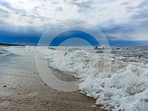 Seascape of the Baltic sea with big foamy waves with yellow sand on the shore and very dark, blue, contrasting clouds above