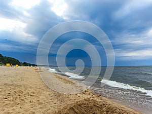 Seascape of the Baltic sea with big foamy waves with yellow sand on the shore and very dark, blue, contrasting clouds above