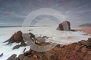 Seascape with beautiful yellow sand beach and majestic rock with a natural cave. Landscape with an overcast sky at sunset.