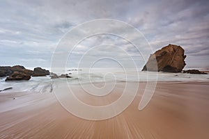 Seascape with beautiful yellow sand beach and majestic rock with a natural cave. Landscape with an overcast sky at sunset. Blue se