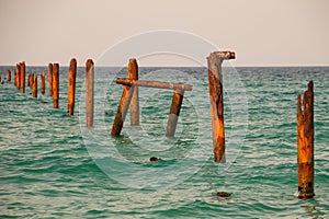 Seascape with blue calm water and rows of Rusty pipes with green algae on summer day. Rusty pipes remaining from old pier.