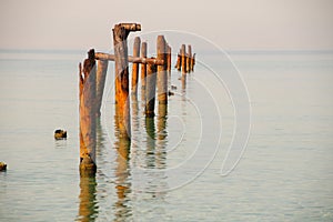 Seascape with blue calm water and rows of Rusty pipes with green algae on summer day. Rusty pipes remaining from old pier.