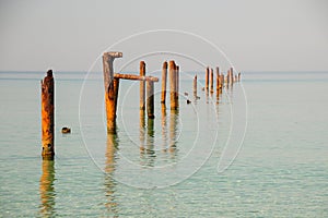 Seascape with blue calm water and rows of Rusty pipes with green algae on summer day. Rusty pipes remaining from old pier.