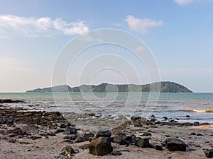 Seascape with boulders and sea waves lash line impact rock on a summer day. Beautiful tropical beach with blue sky and small islan