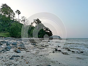 Seascape with boulders and sea waves lash line impact rock on a summer day. Tropical beach with sunset sky and small island view