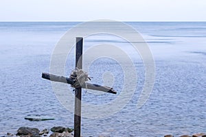Seascape with cross of sticks on rocky beach in overcast day, closeup.