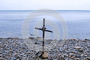 Seascape with cross of sticks on rocky beach in overcast day at sea.