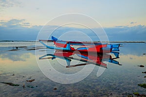 Seascape. Fisherman boat jukung. Traditional fishing boat at the beach during sunset. Cloudy sky. Water reflection. Thomas beach,