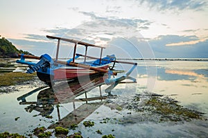 Seascape. Fisherman boat jukung. Traditional fishing boat at the beach during sunset. Cloudy sky. Water reflection. Thomas beach,