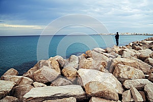 Seascape with huge stones along the coast and a lonely-standing man enjoying the view