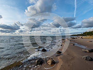 Seascape image of the sea with cloudy sky before sunset,  stones and  of light before sunset, beautiful sunny day and quiet sea.