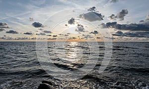 Seascape image of the sea with cloudy sky before sunset,  stones and  of light before sunset, beautiful sunny day and quiet sea.