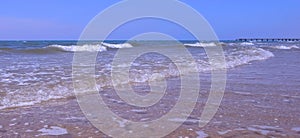 Sea shore with long big waves and pier in distance oin sand beach at sunny day.