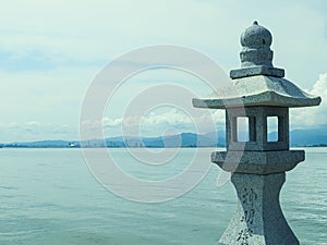 Seascape with mountains in the background and cloudy blue sky with a Japanese stone torii in focus