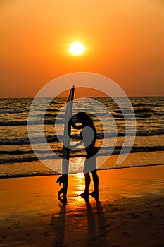 silhouettes of beautiful sexy young women surfer girls in bikinis with surfboards on a beach at sunset in sea, sport activity and