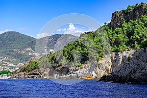 Seascape off the coast of Alanya Turkey with a forest on a steep cliff and a tourist ship in blue water. Beautiful landscape