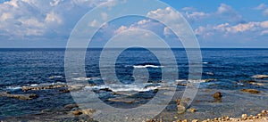 Seascape panorama - natural rock formations at the coast and clear blue water with light waves to the horizon