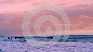 Seascape with pier at sunset. Small waves break on the shore.