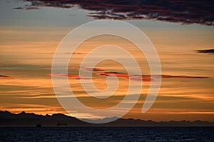 Seascape.  Red dawn sky, Oil drilling platform iÑ‚ Mossel Bay, silhouettes of mountains on the horizon.