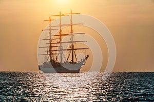 Seascape with sailing ship on sunset. Sailors set sails on masts of ship. White sailing vessel floating in the sea. Copy space.