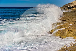 Seascape with sea water spindrift breaking on rocky coastline